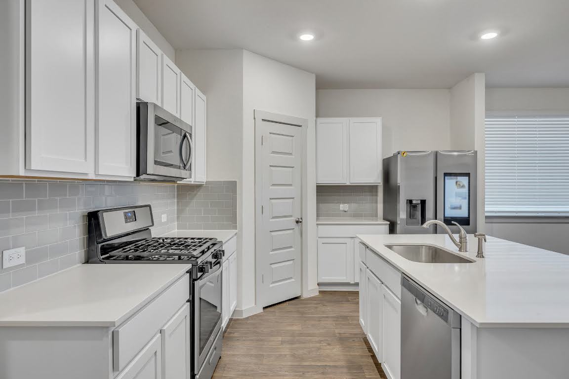 210 Big Cypress Bayou Road Hutto, TX 78634 - Photo 7 of 27 Kitchen featuring appliances with stainless steel finishes, light wood finished floors, white cabinets, tasteful backsplash, and a center island with sink