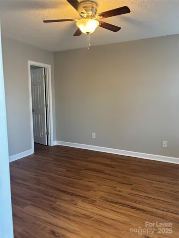 a view of an empty room with wooden floor and a ceiling fan