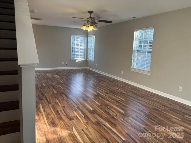 an empty room with wooden floor chandelier fan and windows