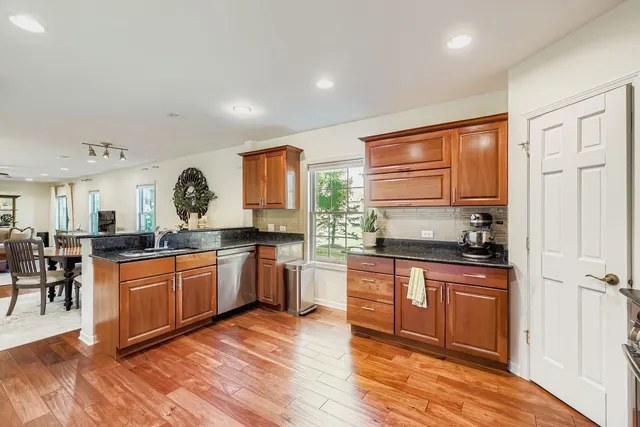 a kitchen with stainless steel appliances granite countertop wooden cabinets a sink a stove a dining table and chairs