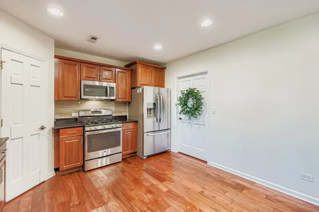 a kitchen with stainless steel appliances granite countertop a refrigerator a stove top oven a sink and dishwasher with wooden floor