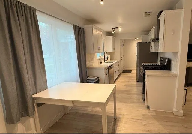 a large kitchen with stainless steel appliances a refrigerator a stove a sink dishwasher and white cabinets with wooden floor