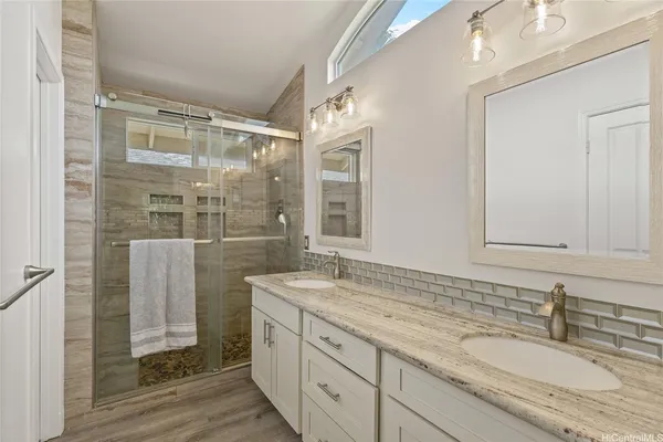 a bathroom with a granite countertop double vanity sink a mirror and a shower