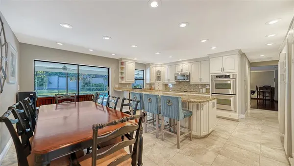 a dining room with stainless steel appliances furniture a large window and a chandelier