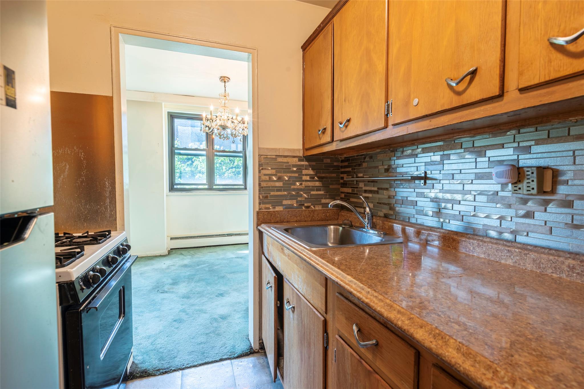 99-35 59th Avenue, Unit 4K Queens, NY 11368 - Photo 15 of 24 Kitchen featuring a baseboard heating unit, gas range, a sink, brown cabinets, and light colored carpet