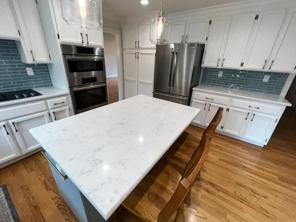 a kitchen with stainless steel appliances kitchen island granite countertop a refrigerator oven a stove with white cabinets and wooden floor