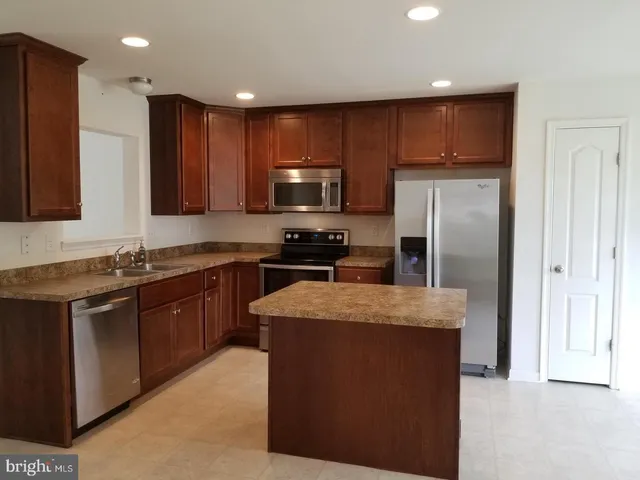 a kitchen with kitchen island granite countertop stainless steel appliances a sink stove refrigerator and cabinets