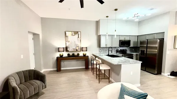 a kitchen with stainless steel appliances kitchen island granite countertop a refrigerator a sink a stove a dining table and chairs with wooden floor