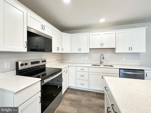 a kitchen with stainless steel appliances a sink a stove top oven a refrigerator with white cabinets and wooden floor