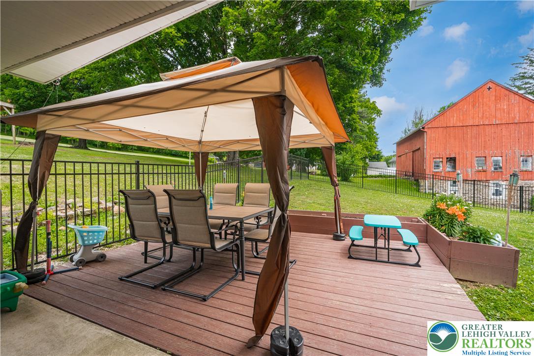 50 Kohls Road Northampton, PA 18067 - Photo 36 of 54 A spacious wooden deck provides ample outdoor living space, featuring a gazebo and views of a verdant yard with a classic red barn.