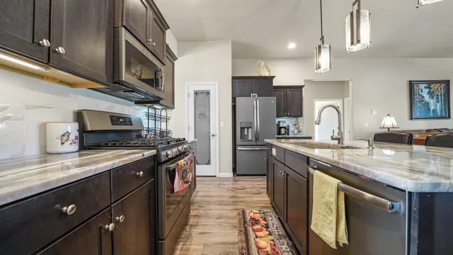 a kitchen with stainless steel appliances granite countertop a sink a stove top oven a refrigerator with wooden cabinets and floor