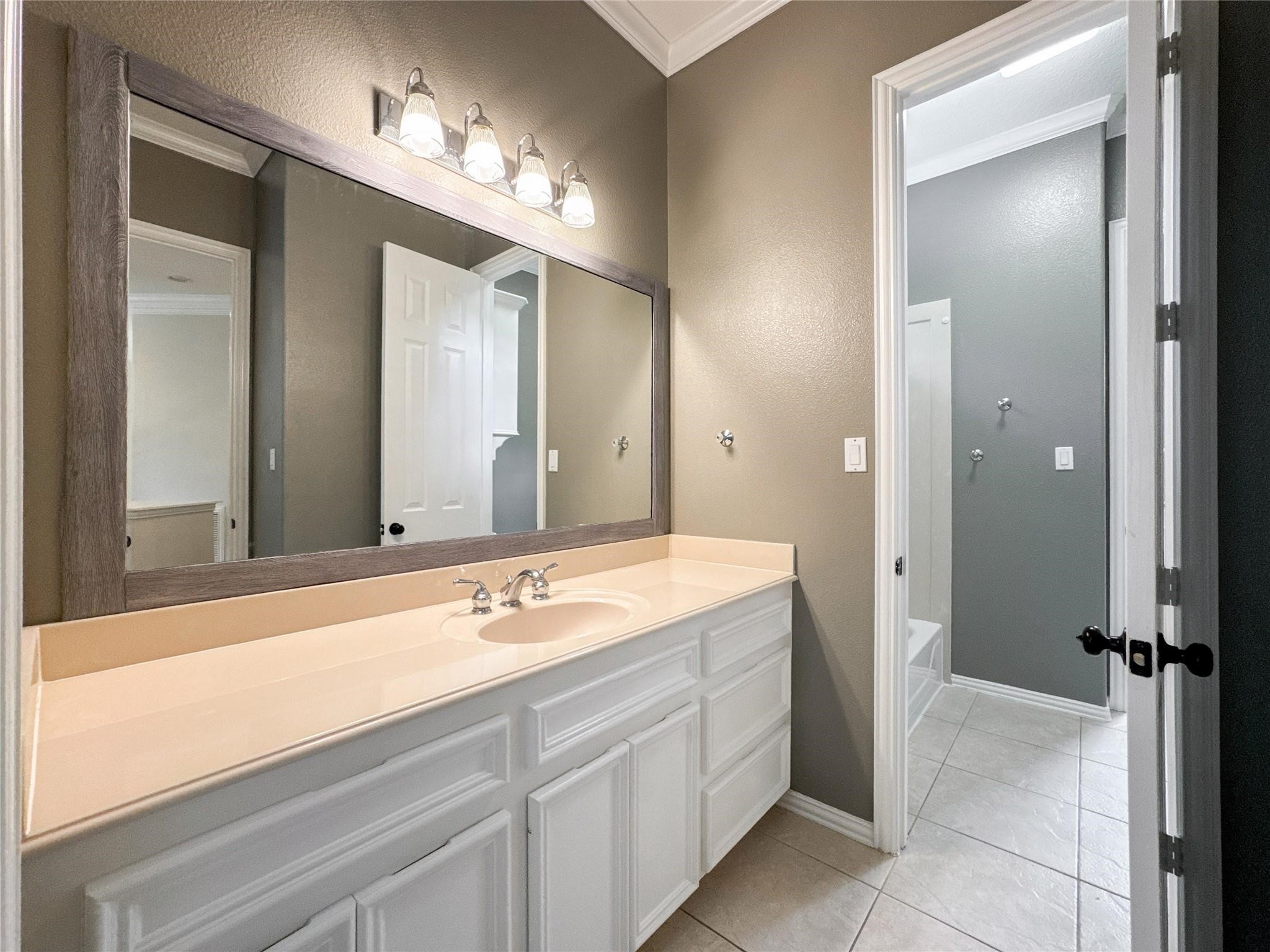 1810 Woerner Road Houston, TX 77090 - Photo 33 of 39 This bathroom features a spacious vanity with a large mirror and modern lighting. It has a neutral color palette with tiled flooring, offering a clean and inviting look.