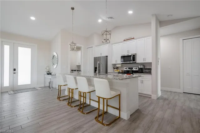 a kitchen with stainless steel appliances granite countertop a refrigerator a microwave oven a stove and white cabinets with wooden floor