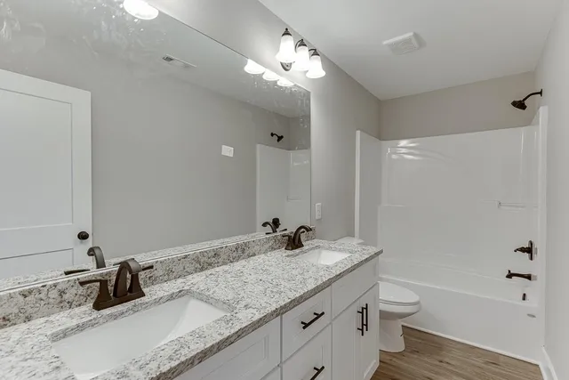 a bathroom with a granite countertop double vanity sink a toilet and shower