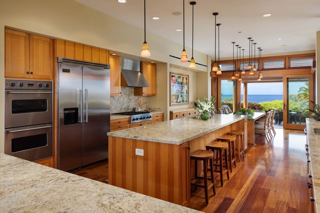 a kitchen with stainless steel appliances kitchen island granite countertop a refrigerator a oven a sink and a dining table with wooden floor