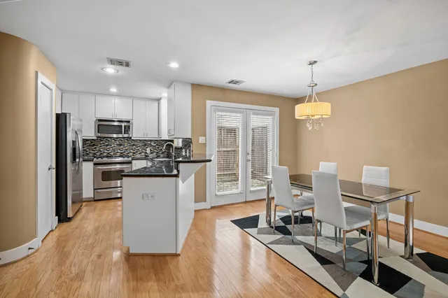 a kitchen with stainless steel appliances kitchen island granite countertop a refrigerator a stove top oven and a dining table with wooden floor