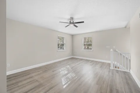 an empty room with wooden floor ceiling fan and windows