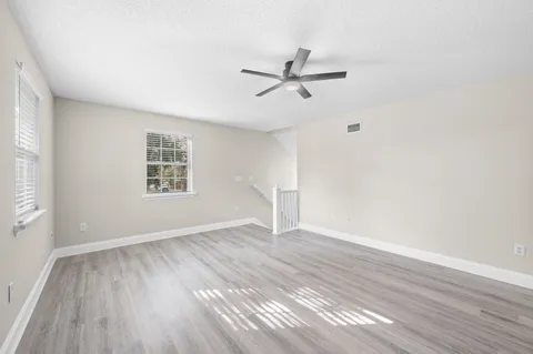 an empty room with wooden floor a ceiling fan and windows