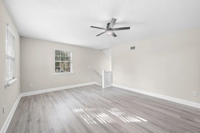 an empty room with wooden floor a ceiling fan and windows