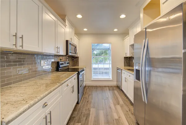 a kitchen with stainless steel appliances granite countertop a refrigerator a sink dishwasher a stove and white countertops with wooden floor