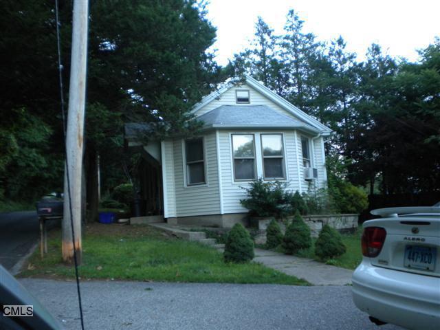 a view of a brick house with a yard plants and large tree