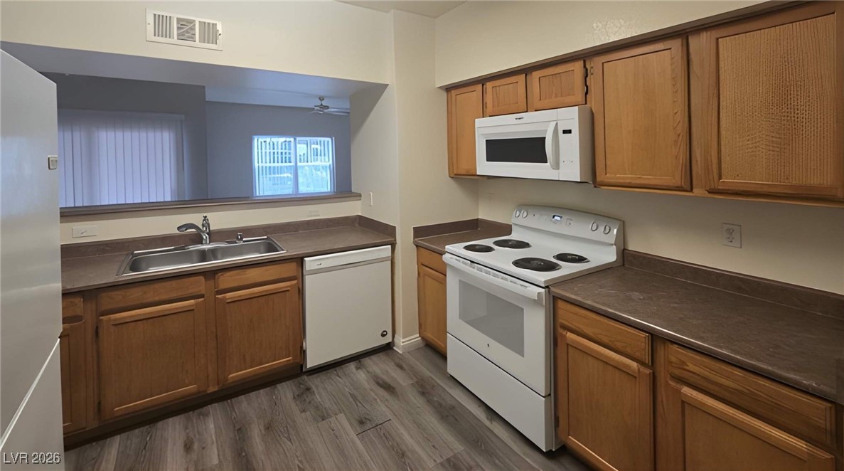 6650 West Warm Springs Road, Unit 1064 Las Vegas, NV 89118 - Photo 4 of 10 Kitchen featuring white appliances, dark wood finished floors, dark countertops, and brown cabinetry