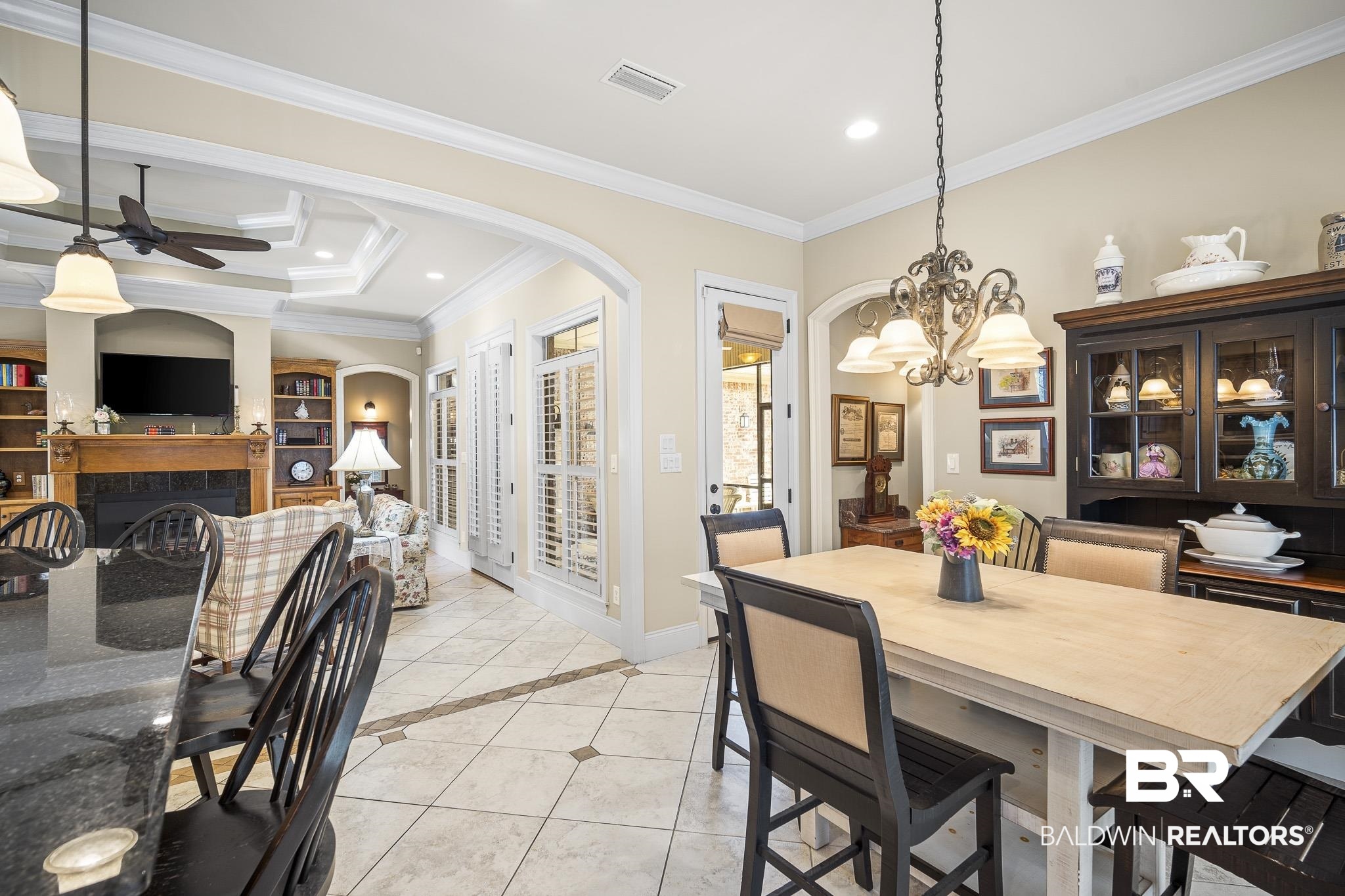 7090 Carson Lane Daphne, AL 36527 - Photo 14 of 37 Dining area featuring light tile patterned flooring, ornamental molding, a tile fireplace, ceiling fan with notable chandelier, and a tray ceiling
