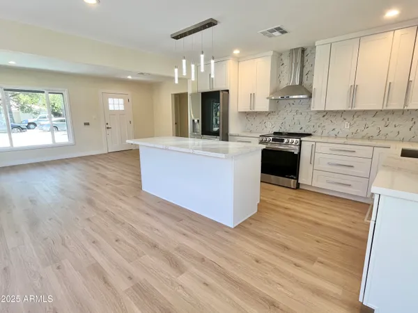 a large kitchen with stainless steel appliances kitchen island granite countertop a stove a sink a refrigerator and a wooden floors