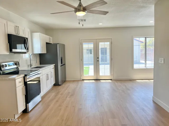 a large kitchen with stainless steel appliances kitchen island a stove a sink dishwasher a refrigerator and white cabinets with wooden floor