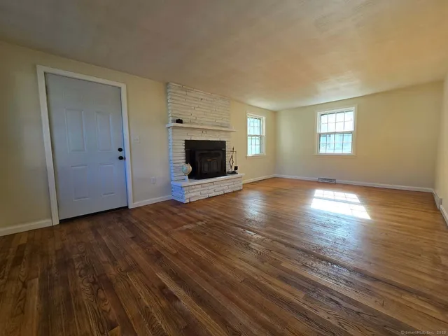 an empty room with wooden floor fireplace and windows