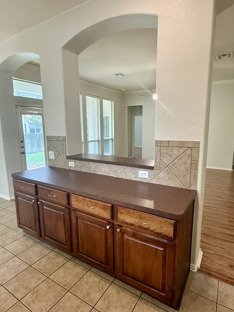 20724 Kearney Hill Road Pflugerville, TX 78660 - Photo 14 of 40 Tile flooring with a rich wood-tone cabinet base featuring a dark countertop, an arched pass-through window with a tile backsplash, and a glass-paneled exterior door