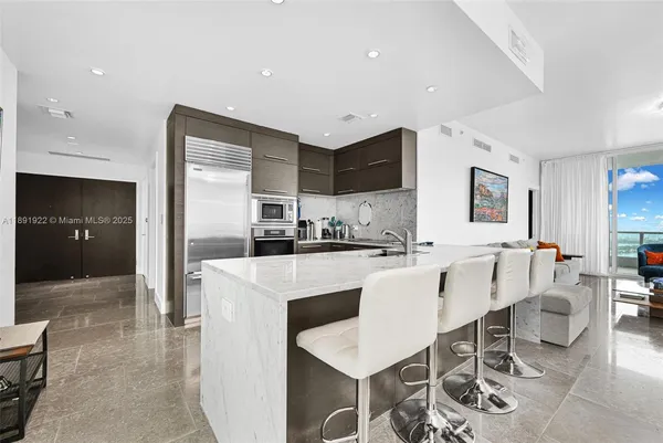 a large white kitchen with stainless steel appliances kitchen island granite countertop a refrigerator a stove a sink a dining table and chairs