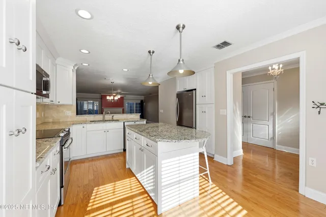 a large kitchen with stainless steel appliances kitchen island granite countertop a sink and a wooden floor