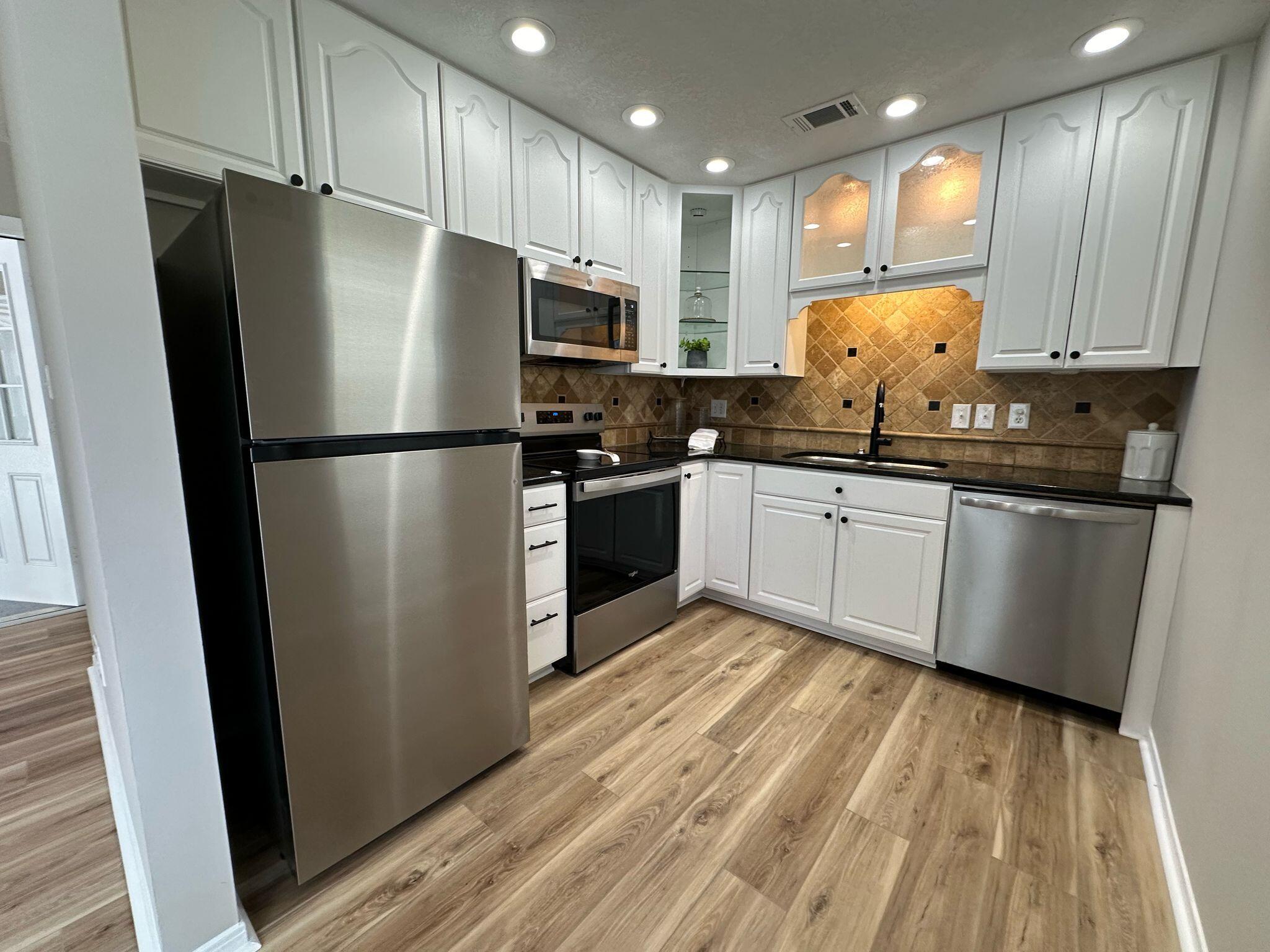 a kitchen with stainless steel appliances a refrigerator a sink a stove a microwave and wooden floors