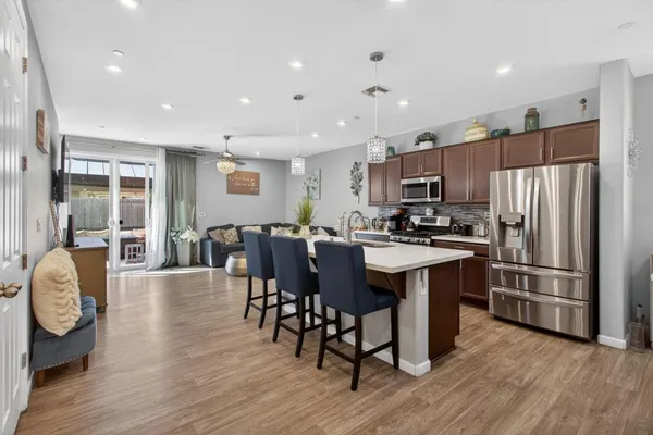 a kitchen with stainless steel appliances granite countertop a refrigerator a stove top oven a sink dishwasher a dining table and chairs with wooden floor
