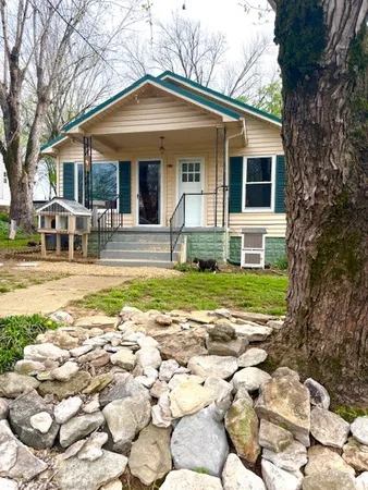 a view of a white house with a small yard and large tree