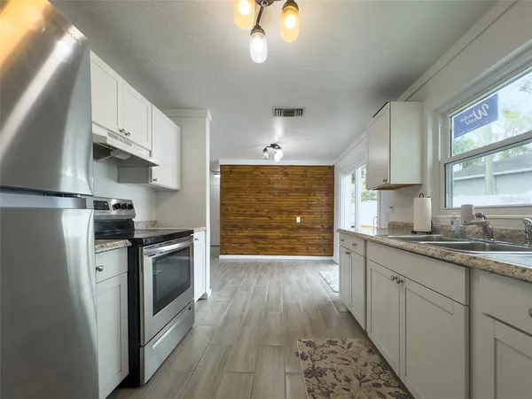 a kitchen with granite countertop a refrigerator a sink dishwasher a stove and white cabinets with wooden floor