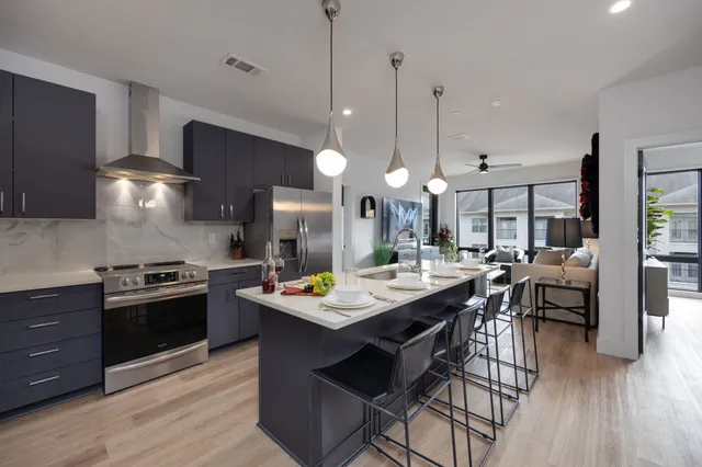 a kitchen with stainless steel appliances a stove a sink a dining table and chairs with wooden floor