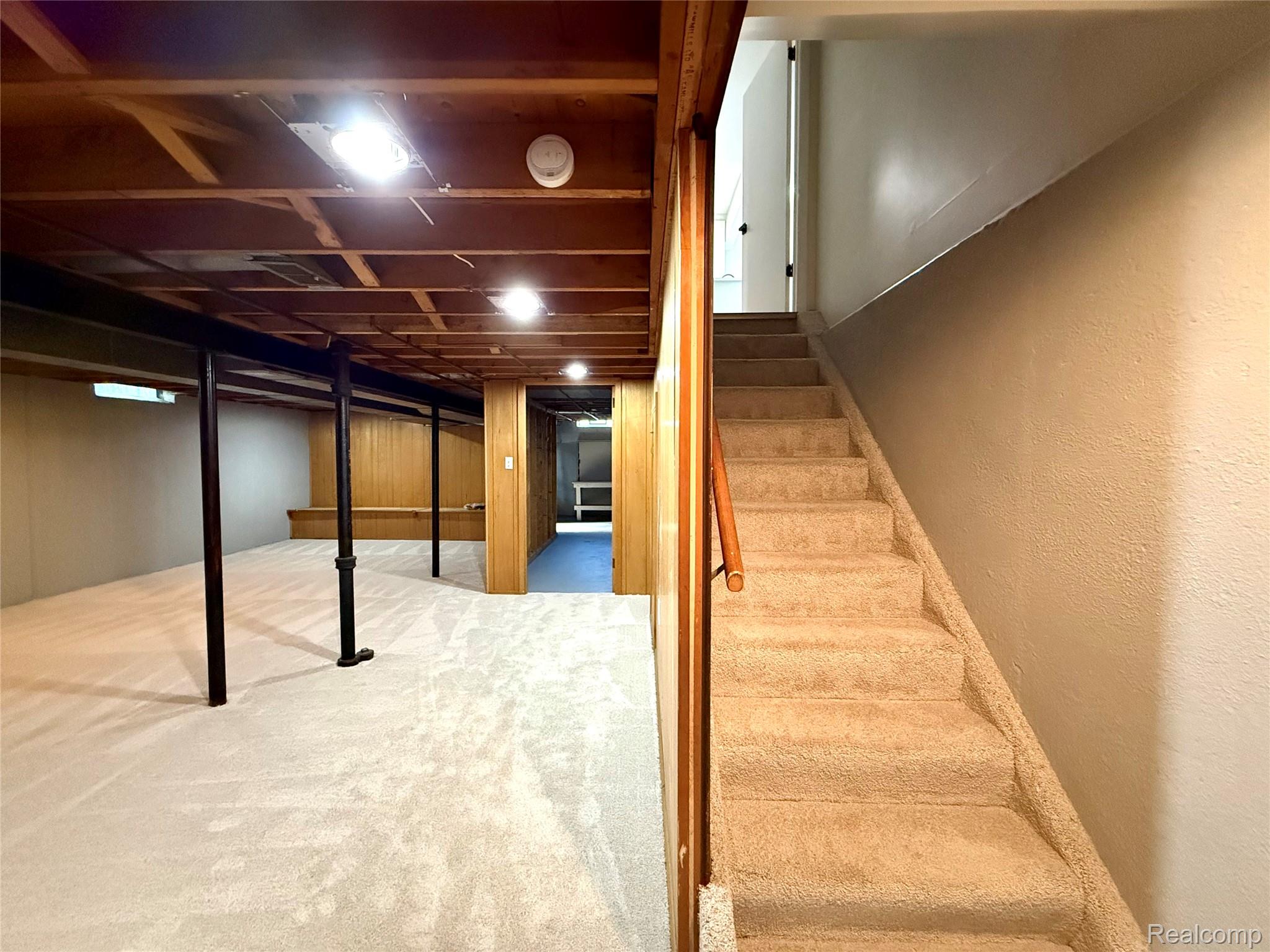 39909 Lynn Street Canton, MI 48187 - Photo 30 of 45 Carpeted staircase with a wood handrail descending to a spacious carpeted lower level featuring exposed wood joist ceiling, recessed lighting, and wood paneling accents