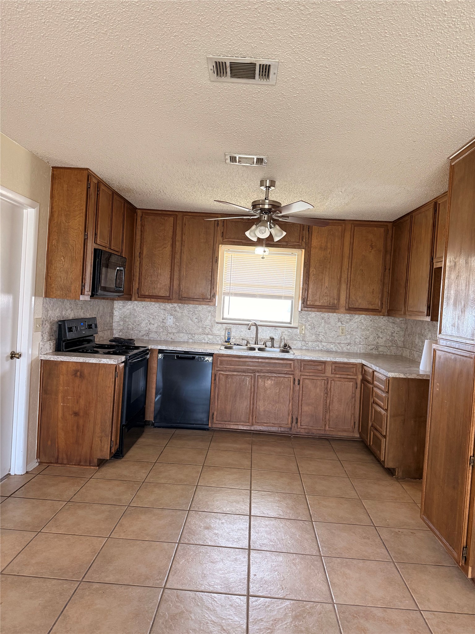 5931 Limmer Loop Hutto, TX 78634 - Photo 10 of 22 Kitchen with wood finish cabinets, black appliances, light countertops, light tile patterned floors, and a ceiling fan