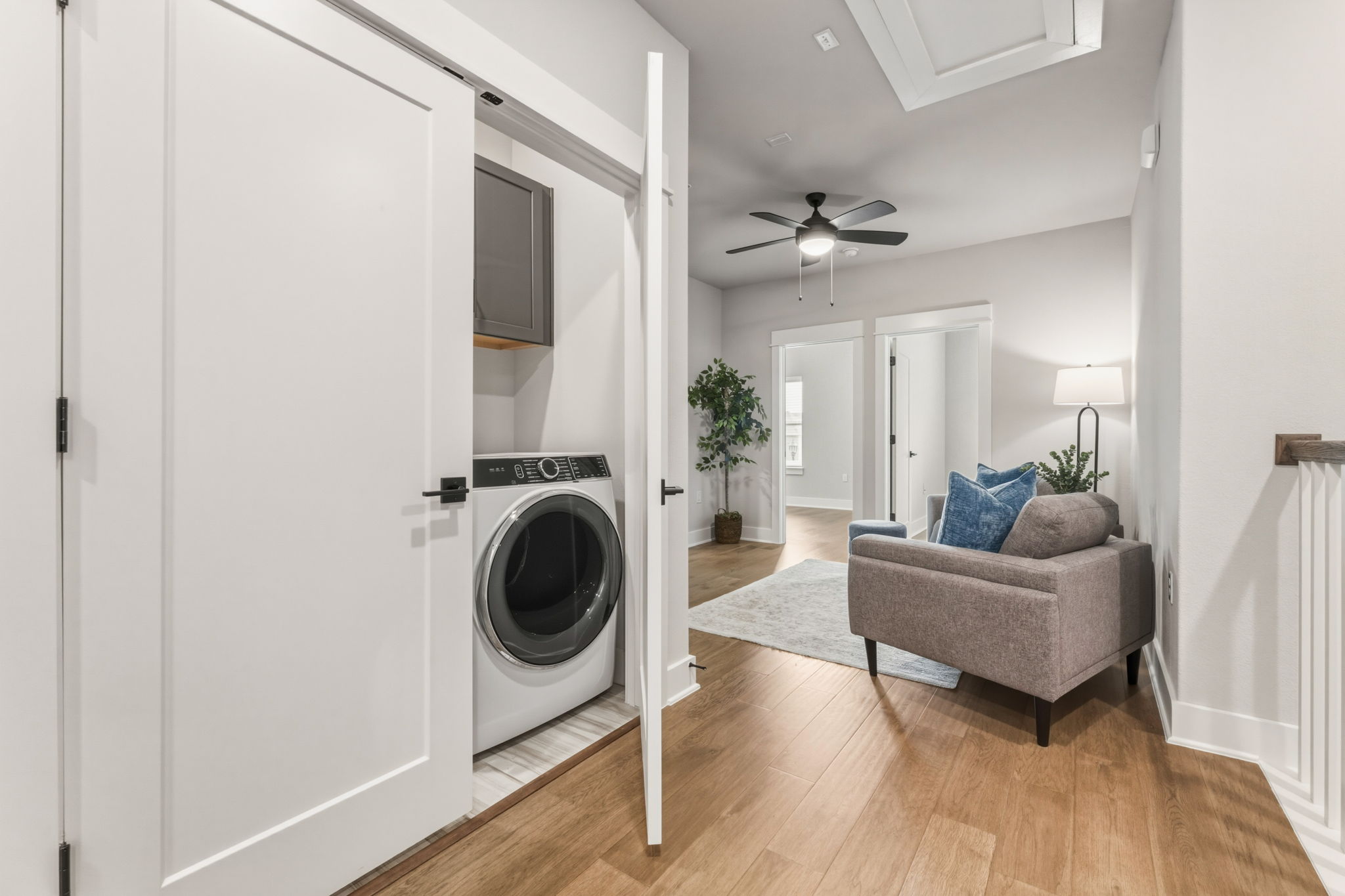2929 Moreno Street Austin, TX 78723 - Photo 27 of 40 Dedicated laundry closet with a front-loading washing machine and upper cabinetry, complemented by wood-finish flooring extending into a bright hall area with a ceiling fan