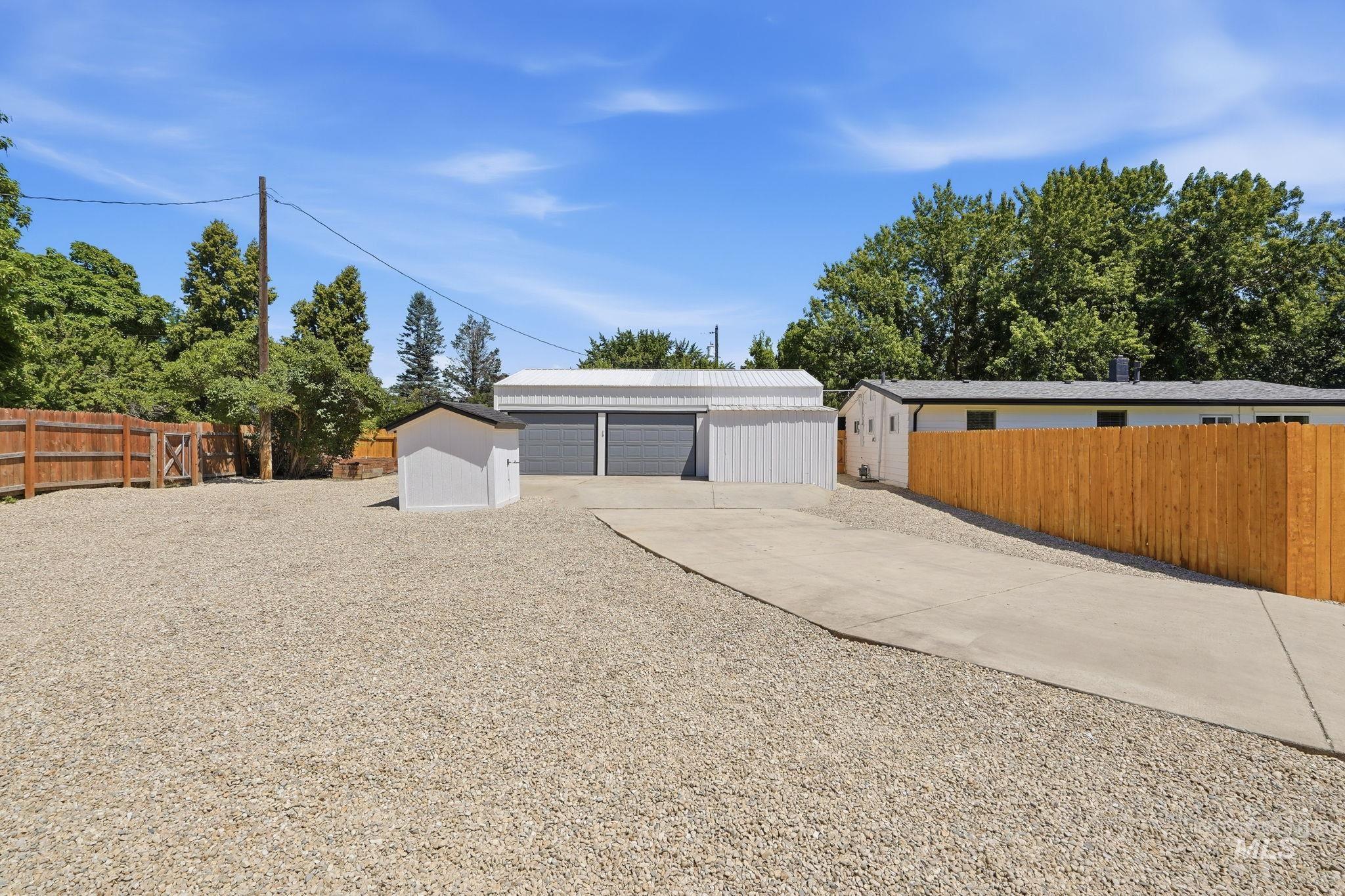 2152 Artesian Road Eagle, ID 83616 - Photo 44 of 50 Gravel yard area featuring a concrete driveway, a freestanding shed, a two-car garage with roll-up doors, and a wood privacy fence