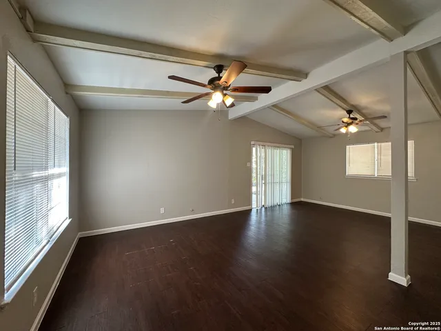 an empty room with wooden floor chandelier fan and windows