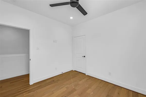 an empty room with wooden floor ceiling fan and window