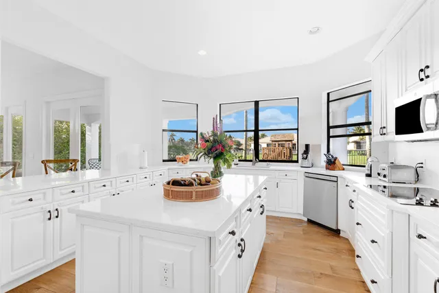 a kitchen with stainless steel appliances a stove top oven a refrigerator a sink dishwasher and white cabinets with wooden floor