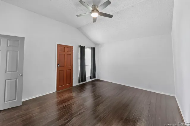 a view of an empty room with wooden floor and a ceiling fan