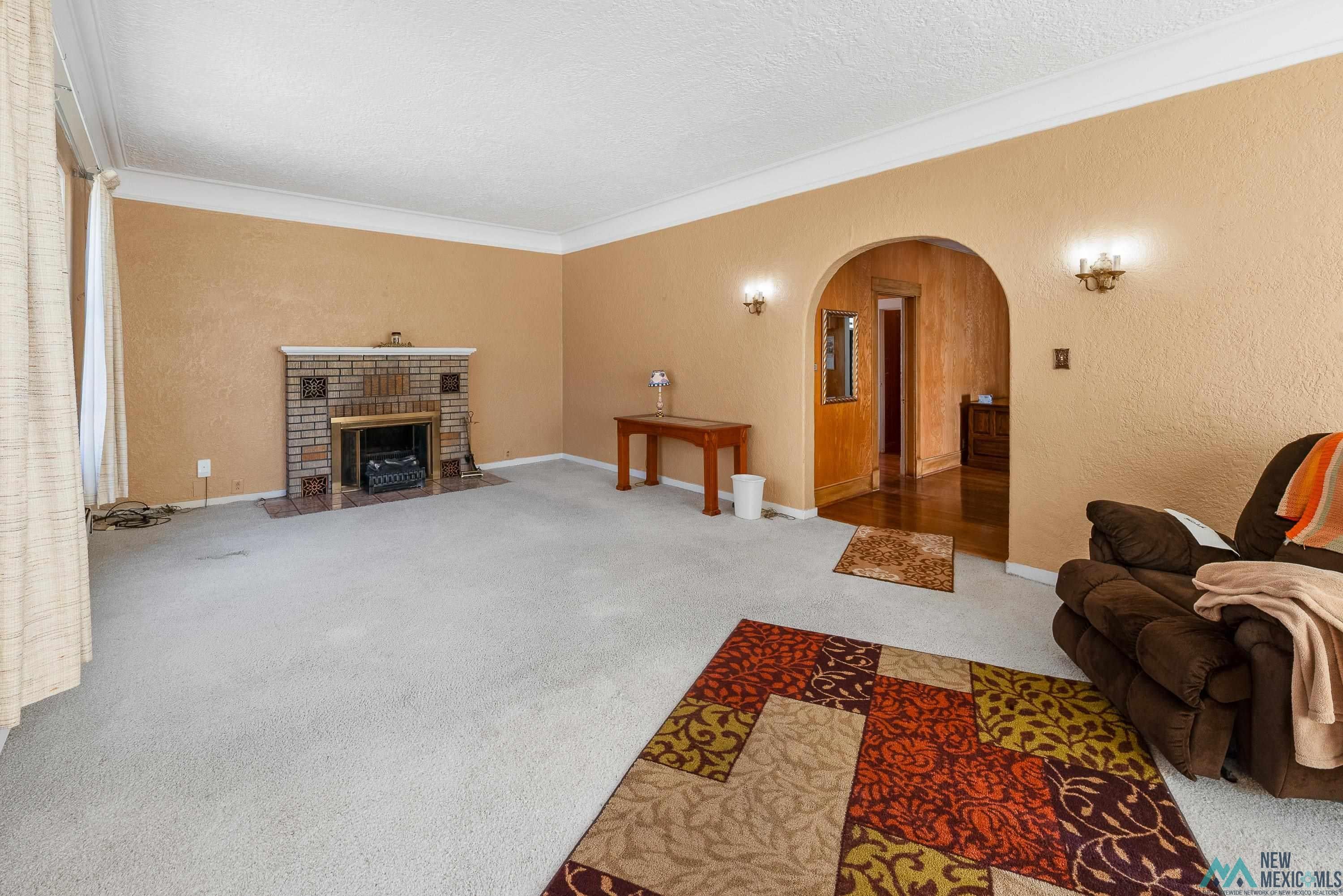 727 South 6th Street Raton, NM 87740 - Photo 5 of 47 Carpeted living area featuring ornamental molding, a textured wall, arched walkways, a fireplace, and a textured ceiling