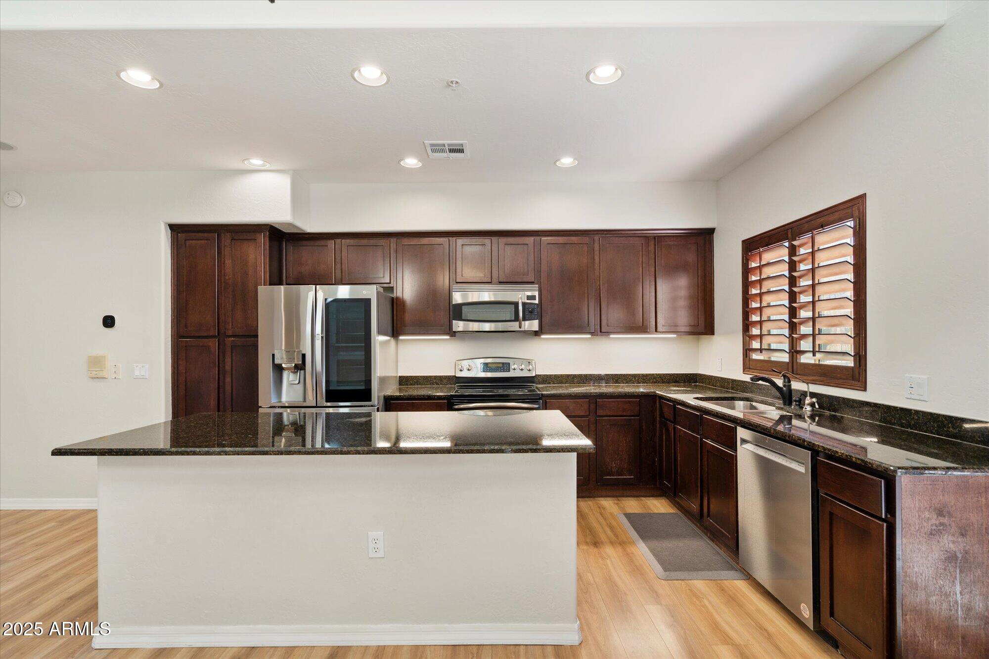 3935 East Rough Rider Road, Unit 1034 Phoenix, AZ 85050 - Photo 4 of 22 a kitchen with kitchen island granite countertop stainless steel appliances a sink a stove a refrigerator cabinets and a counter top space