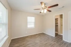 an empty room with wooden floor fan and windows