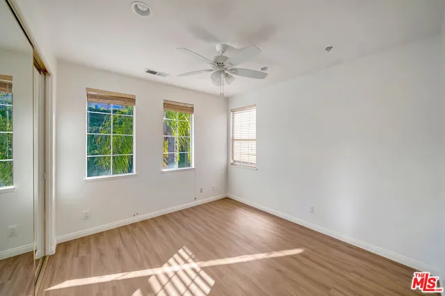 an empty room with wooden floor ceiling fan and windows